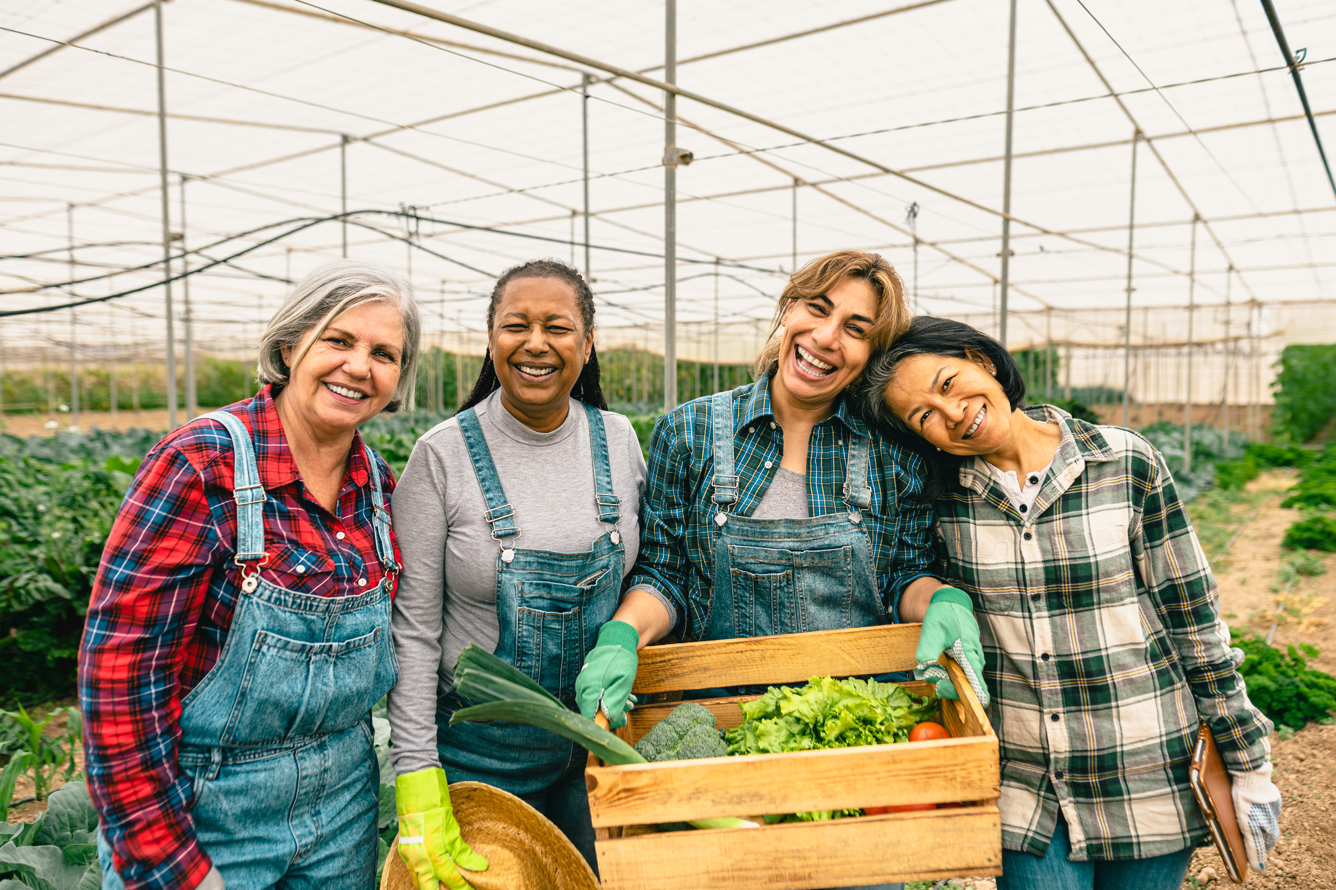 women of various ages under a greenhouse smiling at the camera with a box of vegetables