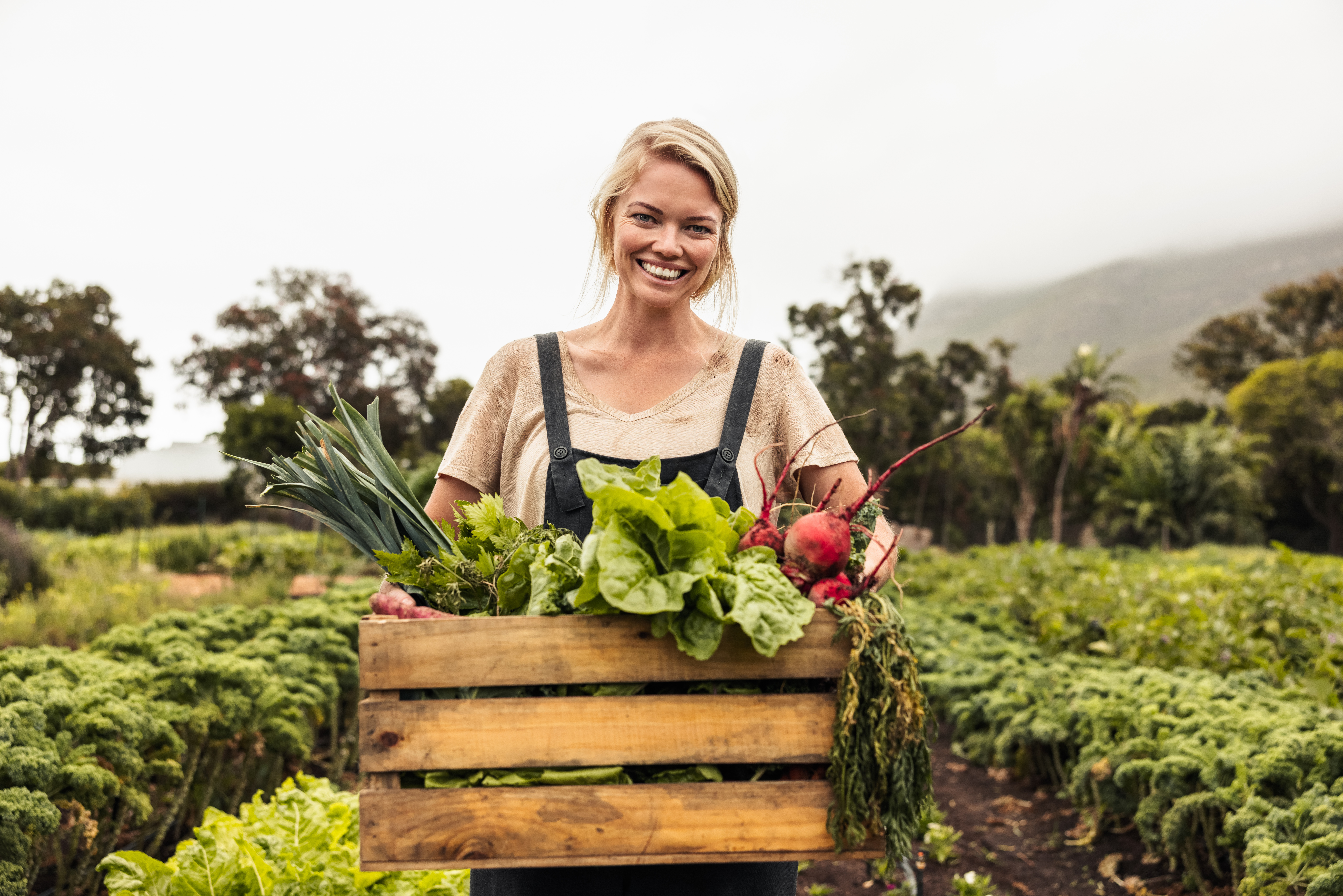 light skinned woman holding a box of freshly poicked vegetables for the camera